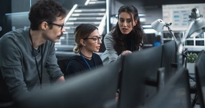 A man and two women in a cyber simulation control room watching a computer and discussing