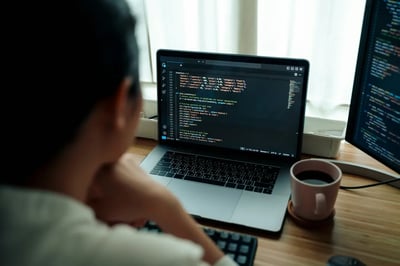 Software developer coding at a workstation with laptop, monitor and coffee cup