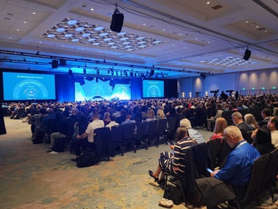 A crowded conference venue from the back with people facing the stage