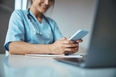 A doctor using a mobile phone while working on a laptop.