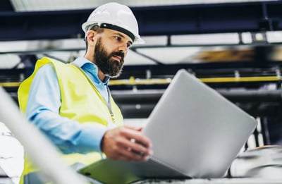 bearded man wearing hard hat looking at computer