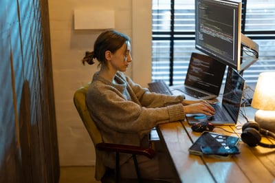 Woman coding at a multi-monitor workstation in a home office
